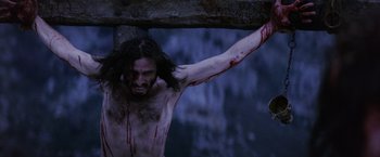 Movie still from “The Passion of the Christ” (2004), directed by Mel Gibson – A man with blood on his face and chest is hanging on a cross; Close Up shot, Low angle