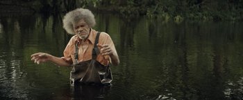 Movie still from “The Peanut Butter Falcon” (2019), directed by Michael Schwartz – An older man in an orange and brown shirt is in the water; Medium shot, Over the shoulder angle
