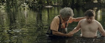 Movie still from “The Peanut Butter Falcon” (2019), directed by Michael Schwartz – An older man in the water holding a piece of wood; Medium shot, Over the shoulder angle
