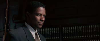 Movie still from “The Pelican Brief” (1993), directed by Alan J. Pakula – A man in a suit and tie in front of some books; Close Up shot, Over the shoulder angle