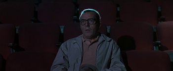 Movie still from “The Pelican Brief” (1993), directed by Alan J. Pakula – A man with glasses is sitting in a movie theater; Medium shot, Low angle