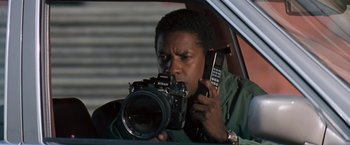 Movie still from “The Pelican Brief” (1993), directed by Alan J. Pakula – A man holding a camera while holding a phone; Close Up shot, Low angle