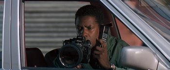 Movie still from “The Pelican Brief” (1993), directed by Alan J. Pakula – A man in a car holding a camera and holding a cell phone; Close Up shot, Low angle