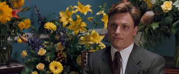 Movie still from “The Pelican Brief” (1993), directed by Alan J. Pakula – A man in a suit standing in front of flowers; Close Up shot, Over the shoulder angle