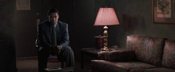Movie still from “The Pelican Brief” (1993), directed by Alan J. Pakula – A man in a suit sitting in front of a lamp in a dark room; Medium shot, Over the shoulder angle