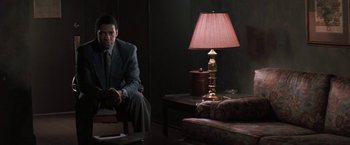 Movie still from “The Pelican Brief” (1993), directed by Alan J. Pakula – A man in a suit sitting in front of a lamp in a dark room; Medium shot, Over the shoulder angle