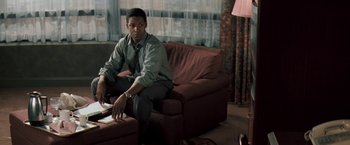 Movie still from “The Pelican Brief” (1993), directed by Alan J. Pakula – A man sitting on top of a couch in a living room; Medium shot, High angle