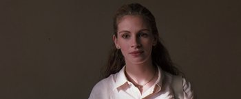 Movie still from “The Pelican Brief” (1993), directed by Alan J. Pakula – A young woman wearing a white dress shirt and a necklace; Close Up shot, Low angle