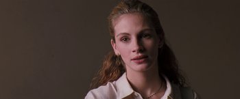 Movie still from “The Pelican Brief” (1993), directed by Alan J. Pakula – A young woman with long brown hair wearing a white dress shirt; Close Up shot, Low angle