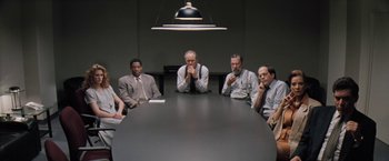 Movie still from “The Pelican Brief” (1993), directed by Alan J. Pakula – A group of people sitting around a table in front of a lamp; Wide shot, High angle