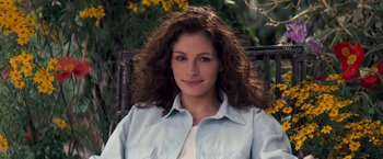 Movie still from “The Pelican Brief” (1993), directed by Alan J. Pakula – A woman sitting in a chair in front of some flowers; Close Up shot, High angle