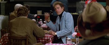 Movie still from “The People vs. Larry Flynt” (1996), directed by Milos Forman – A man sitting at a table holding a glass of wine; Medium shot, Over the shoulder angle