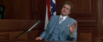 Movie still from “The People vs. Larry Flynt” (1996), directed by Milos Forman – A man wearing a suit and tie sitting at a table; Medium shot, Low angle