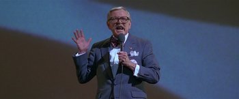 Movie still from “The People vs. Larry Flynt” (1996), directed by Milos Forman – An older man wearing a suit and tie while holding a microphone; Medium shot, High angle