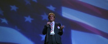 Movie still from “The People vs. Larry Flynt” (1996), directed by Milos Forman – A man in a suit and tie holding a microphone; Medium shot, Low angle