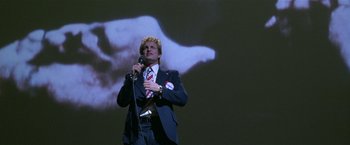 Movie still from “The People vs. Larry Flynt” (1996), directed by Milos Forman – A man in a suit and tie holding a microphone; Medium shot, Low angle