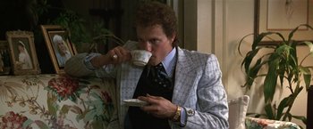 Movie still from “The People vs. Larry Flynt” (1996), directed by Milos Forman – A man drinking a cup of coffee while sitting on a couch; Medium shot, Low angle