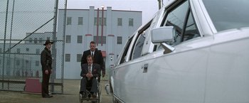 Movie still from “The People vs. Larry Flynt” (1996), directed by Milos Forman – A man in a wheelchair with another man in a suit in front of a car; Wide shot, Low angle