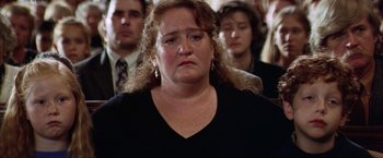 Movie still from “The Perfect Storm” (2000), directed by Wolfgang Petersen – A person wearing a black shirt with people in the background; Close Up shot, High angle