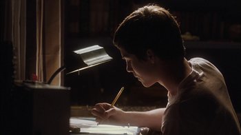 Movie still from “The Perks of Being a Wallflower” (2012), directed by Stephen Chbosky – A young man writing on a piece of paper while sitting at a desk; Medium shot, Low angle