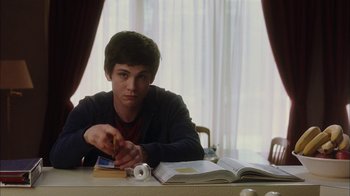 Movie still from “The Perks of Being a Wallflower” (2012), directed by Stephen Chbosky – A young man sitting at a table with a book; Medium shot, Over the shoulder angle