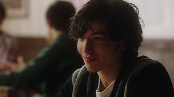 Movie still from “The Perks of Being a Wallflower” (2012), directed by Stephen Chbosky – A young man with long black hair smiles for the camera; Close Up shot, Over the shoulder angle