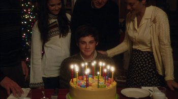 Movie still from “The Perks of Being a Wallflower” (2012), directed by Stephen Chbosky – A boy sitting in front of a birthday cake with lit candles on it; Medium shot, High angle
