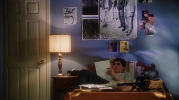 Movie still from “The Perks of Being a Wallflower” (2012), directed by Stephen Chbosky – A man sitting on a bed in a room with many pictures on the wall; Wide shot, High angle