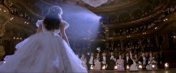 Movie still from “The Phantom of the Opera” (2004), directed by Joel Schumacher – A woman in a white dress standing in front of an audience; Wide shot, Over the shoulder angle