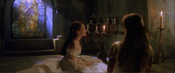 Movie still from “The Phantom of the Opera” (2004), directed by Joel Schumacher – A woman sitting on top of a bed next to candles; Medium shot, High angle