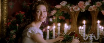 Movie still from “The Phantom of the Opera” (2004), directed by Joel Schumacher – A young woman in a white dress holding a mirror and candles; Medium shot, Over the shoulder angle