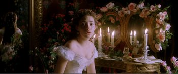 Movie still from “The Phantom of the Opera” (2004), directed by Joel Schumacher – A woman in a white dress sitting in front of a mirror; Medium shot, Over the shoulder angle