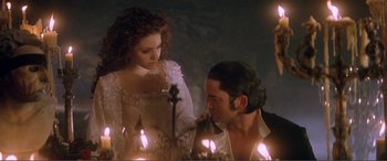 Movie still from “The Phantom of the Opera” (2004), directed by Joel Schumacher – A man and a woman are standing in front of lit candles; Medium shot, Over the shoulder angle