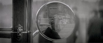 Movie still from “The Phantom of the Opera” (2004), directed by Joel Schumacher – A man in a top hat is reflected in a round mirror; Extreme Close Up shot, Over the shoulder angle