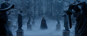 Movie still from “The Phantom of the Opera” (2004), directed by Joel Schumacher – A man in a black cape standing in front of statues in the fog; Wide shot, High angle