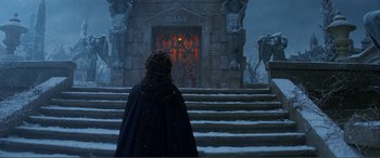 A woman in a black cloak standing in front of a building