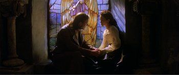 Movie still from “The Phantom of the Opera” (2004), directed by Joel Schumacher – A man and a woman sitting on a chair in front of a stained glass window; Medium shot, Low angle