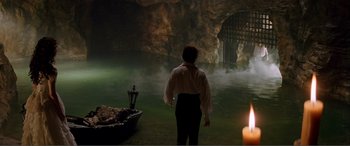 Movie still from “The Phantom of the Opera” (2004), directed by Joel Schumacher – A man standing in front of a cave with a candle; Extreme Wide shot, High angle