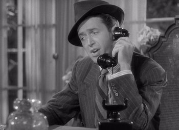 Movie still from “The Philadelphia Story” (1940), directed by George Cukor – A man wearing a suit and hat talking on a phone; Close Up shot, High angle