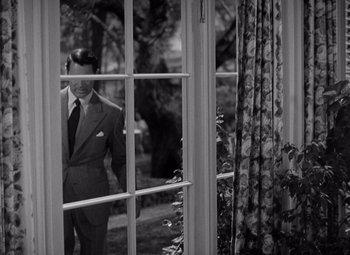 Movie still from “The Philadelphia Story” (1940), directed by George Cukor – A black and white photo of a man in a suit looking out of a window; Medium shot, High angle