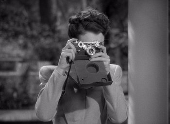 Movie still from “The Philadelphia Story” (1940), directed by George Cukor – A black and white photo of a woman taking a picture with an old camera; Medium shot, Over the shoulder angle