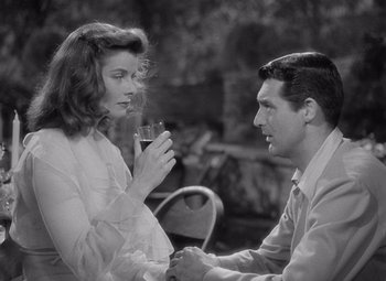Movie still from “The Philadelphia Story” (1940), directed by George Cukor – A man and a woman are holding hands and drinking wine; Medium shot, Over the shoulder angle