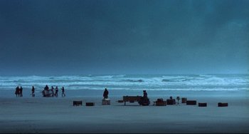Movie still from “The Piano” (1993), directed by Jane Campion – People are sitting on benches on the beach; Extreme Wide shot, High angle