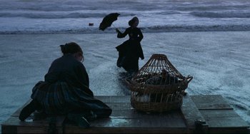Movie still from “The Piano” (1993), directed by Jane Campion – Two women on the beach one with an umbrella and the other with a bird cage; Extreme Wide shot, High angle