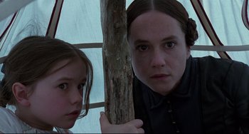 Movie still from “The Piano” (1993), directed by Jane Campion – Two young girls standing next to each other near a wooden pole; Close Up shot, Low angle