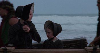 Movie still from “The Piano” (1993), directed by Jane Campion – Two people in black clothes and hats near a body of water; Medium shot, Low angle