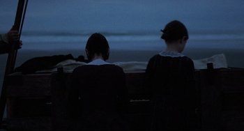 Movie still from “The Piano” (1993), directed by Jane Campion – Two people sitting on a bench looking out at the ocean at night; Medium shot, Over the shoulder angle