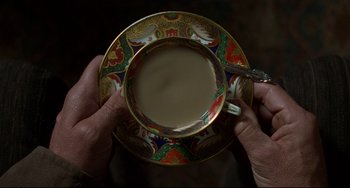 Movie still from “The Piano” (1993), directed by Jane Campion – A person holding a cup of coffee over a plate; Extreme Close Up shot, Overhead angle