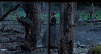 Movie still from “The Piano” (1993), directed by Jane Campion – A woman in a black dress standing next to a tree; Wide shot, Over the shoulder angle