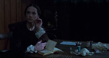 Movie still from “The Piano” (1993), directed by Jane Campion – A woman sitting at a table holding a book; Medium shot, High angle